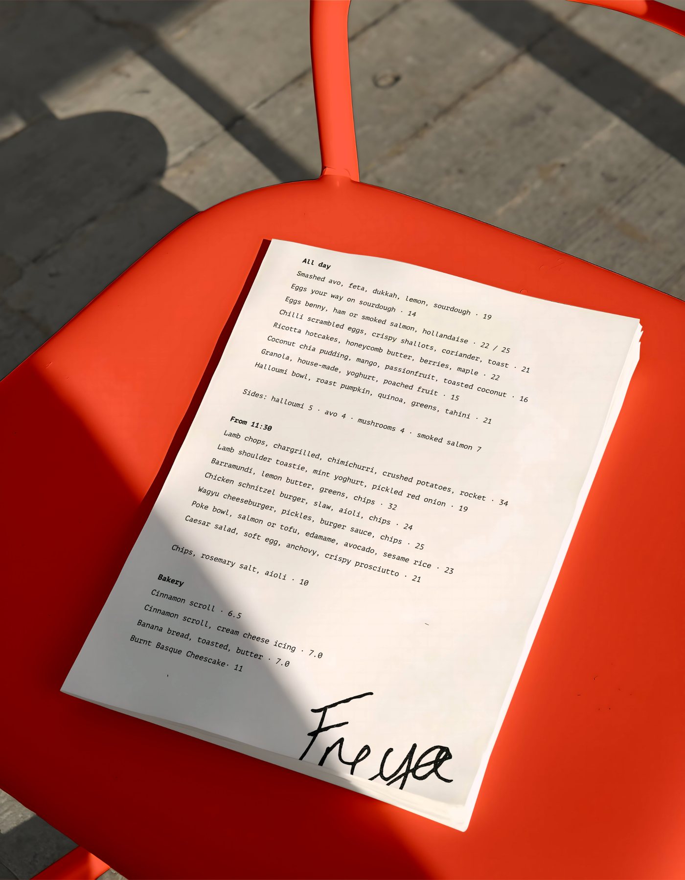 The Freya all-day menu, photographed on an orange café chair in sunlight.